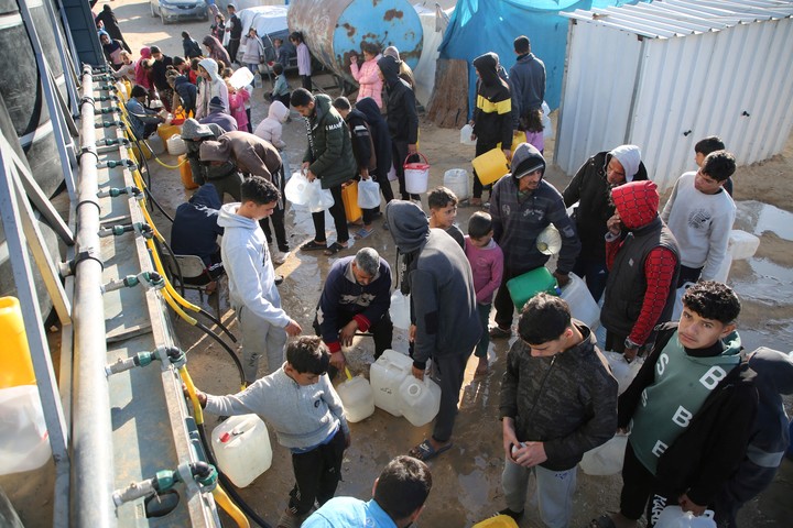 Familias palestinan cargan bidones con agua en un campamento para desplazados en Khan Younis, este jueves. Foto: REUTERS   